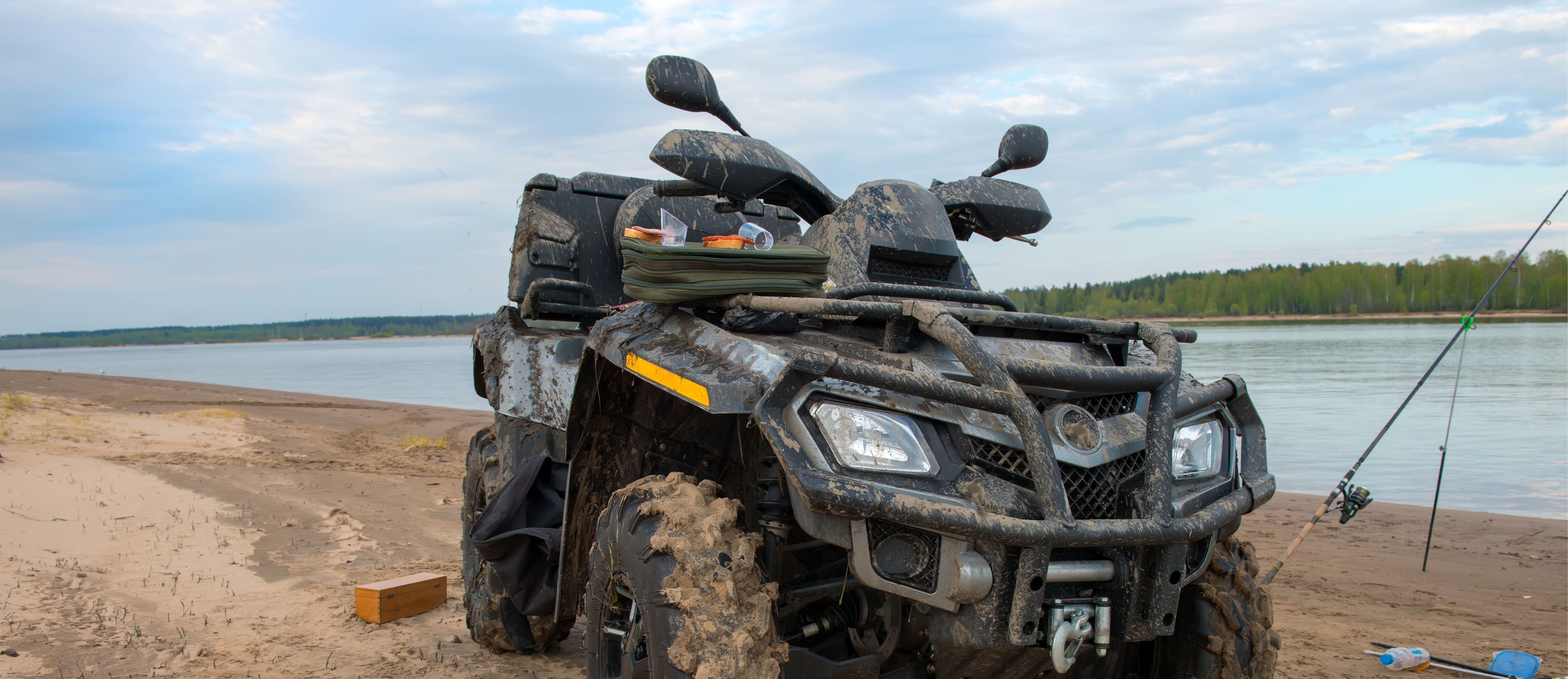Muddy ATV parked on a sandy riverbank