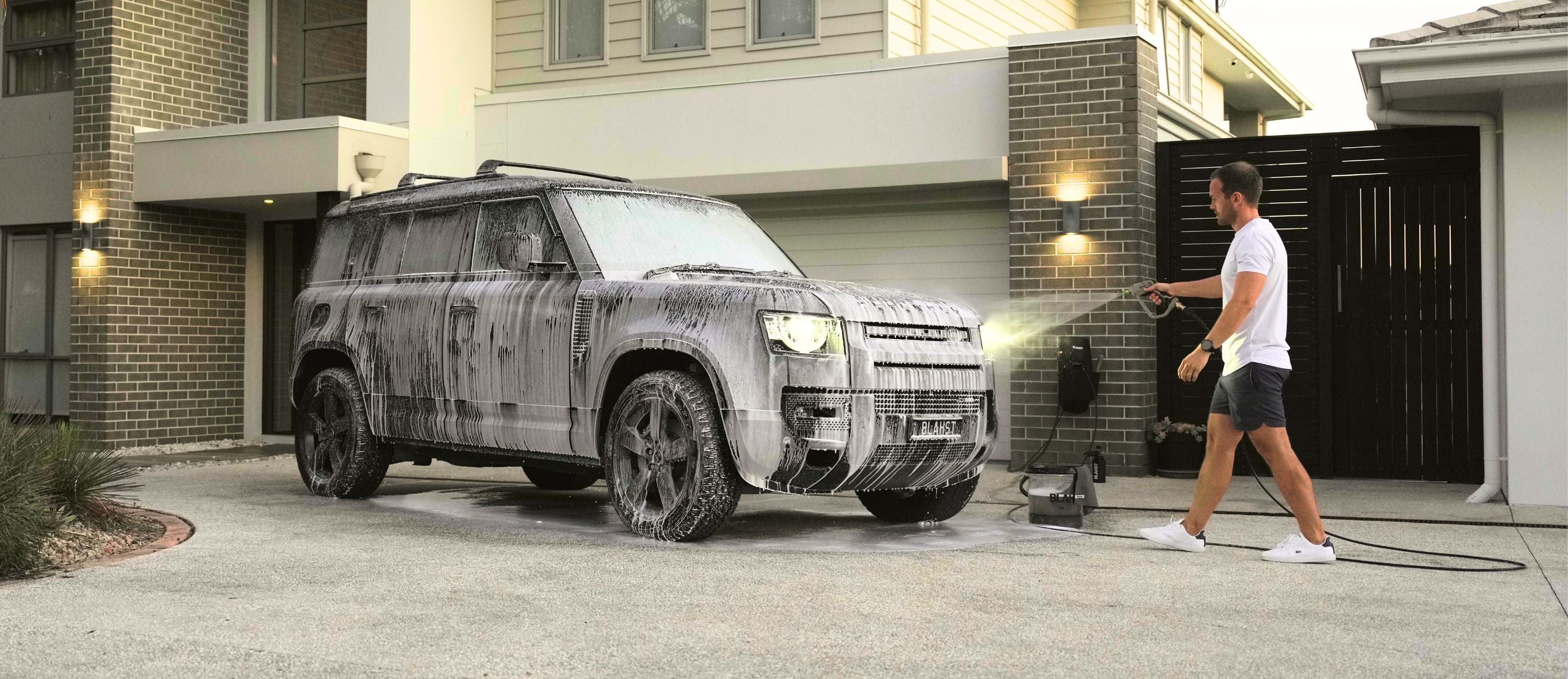 pressure washing a foam-covered SUV in a driveway